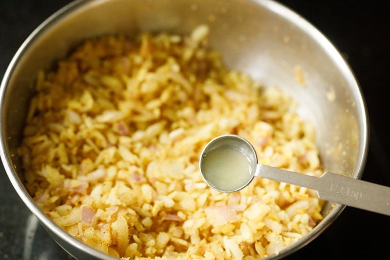 lemon juice in a measuring spoon on top of bowl with poha mixture.