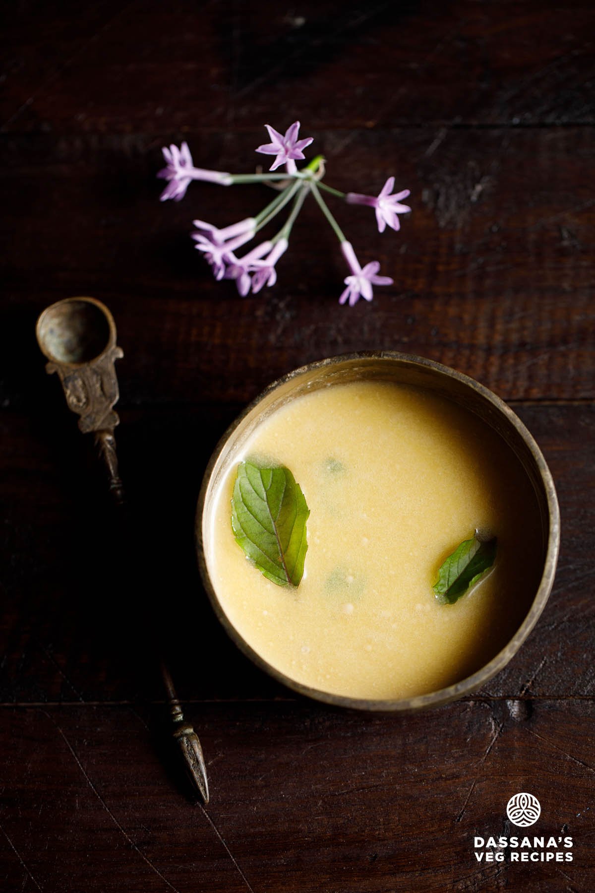 Bowl of panchamrit with tulsi leaves and a decorative brass spoon by the side.