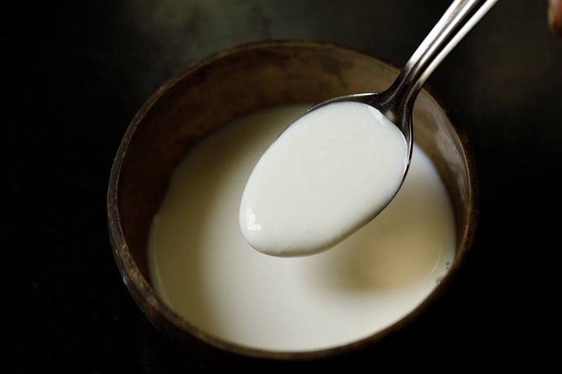 Spoonful of creamy white yogurt being added to milk in bowl.