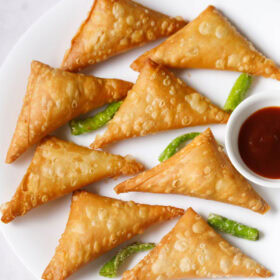Crispy patti samosa with green chilies and tamarind chutney on a white plate.