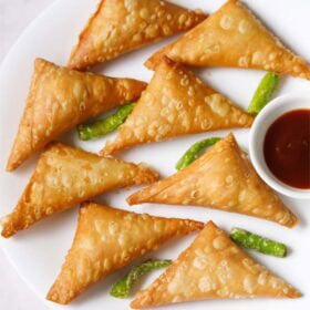 Crispy patti samosa or onion samosa with dipping tamarind chutney and green chillies on a white plate.