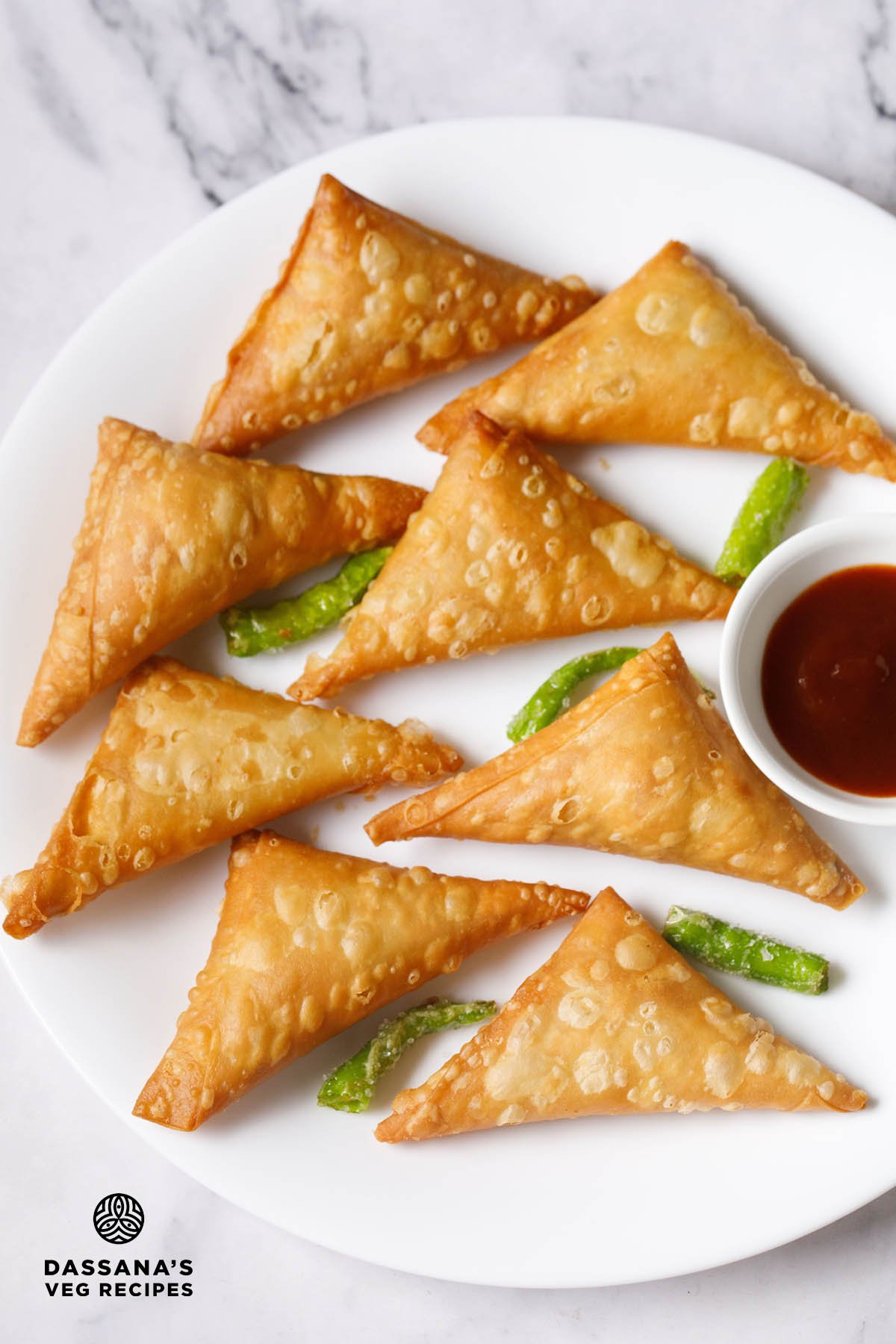 Crispy patti samosa with green chilies and tamarind chutney on a white plate.