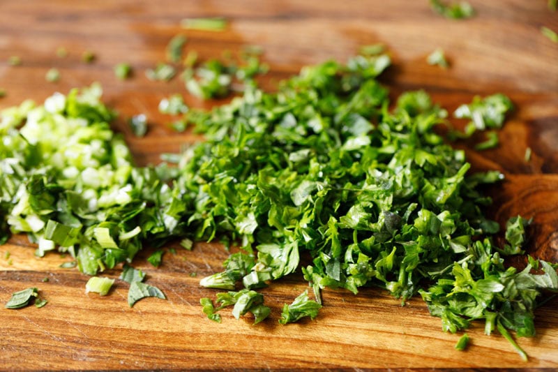 Chopped green herbs on wooden board.