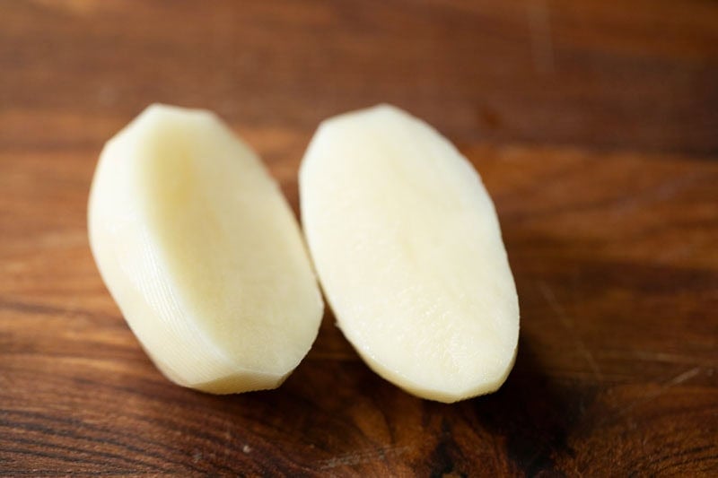Two halved raw potatoes on wooden board.