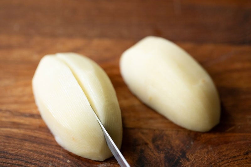 Two peeled and halved potatoes being sliced.