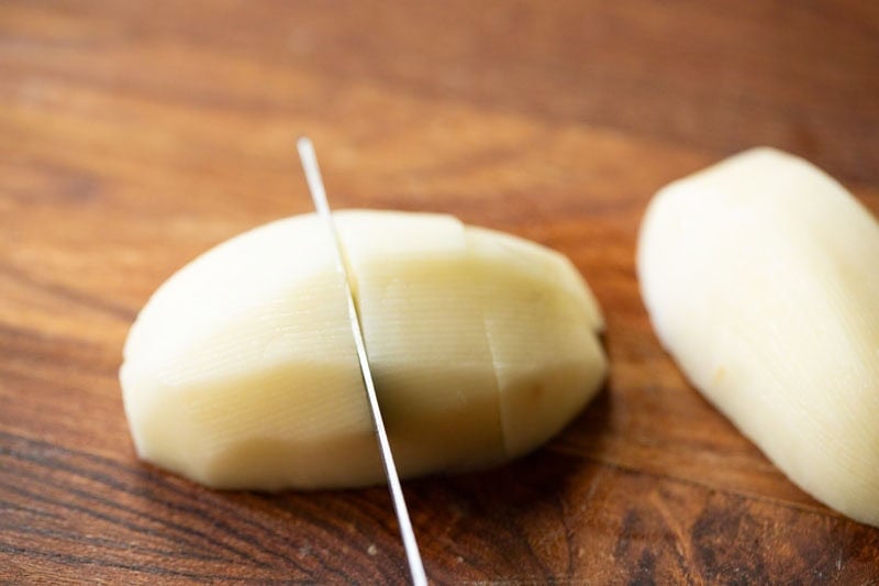 Peeled potato being sliced on wooden board.