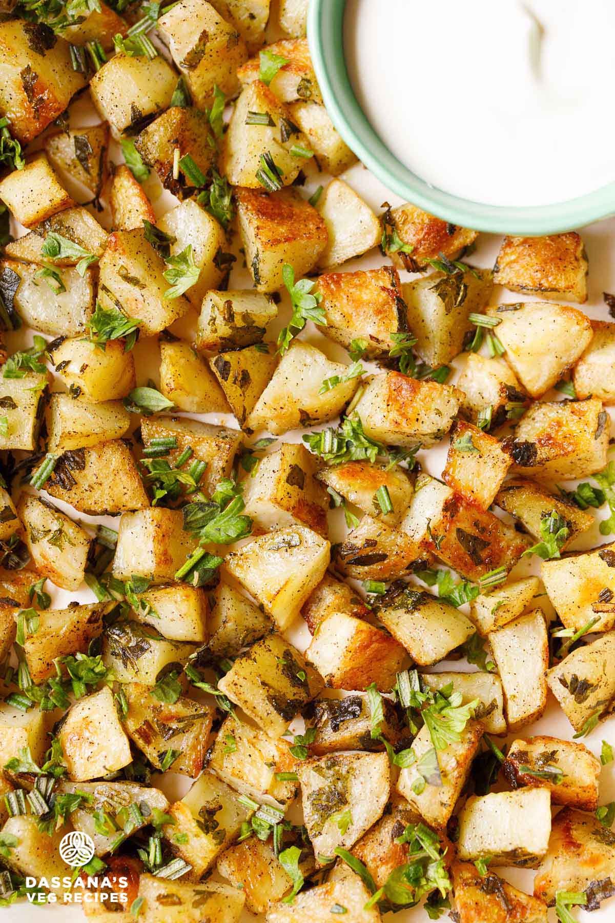 roasted potatoes garnished with parsley on baking tray with a side of yogurt dip.