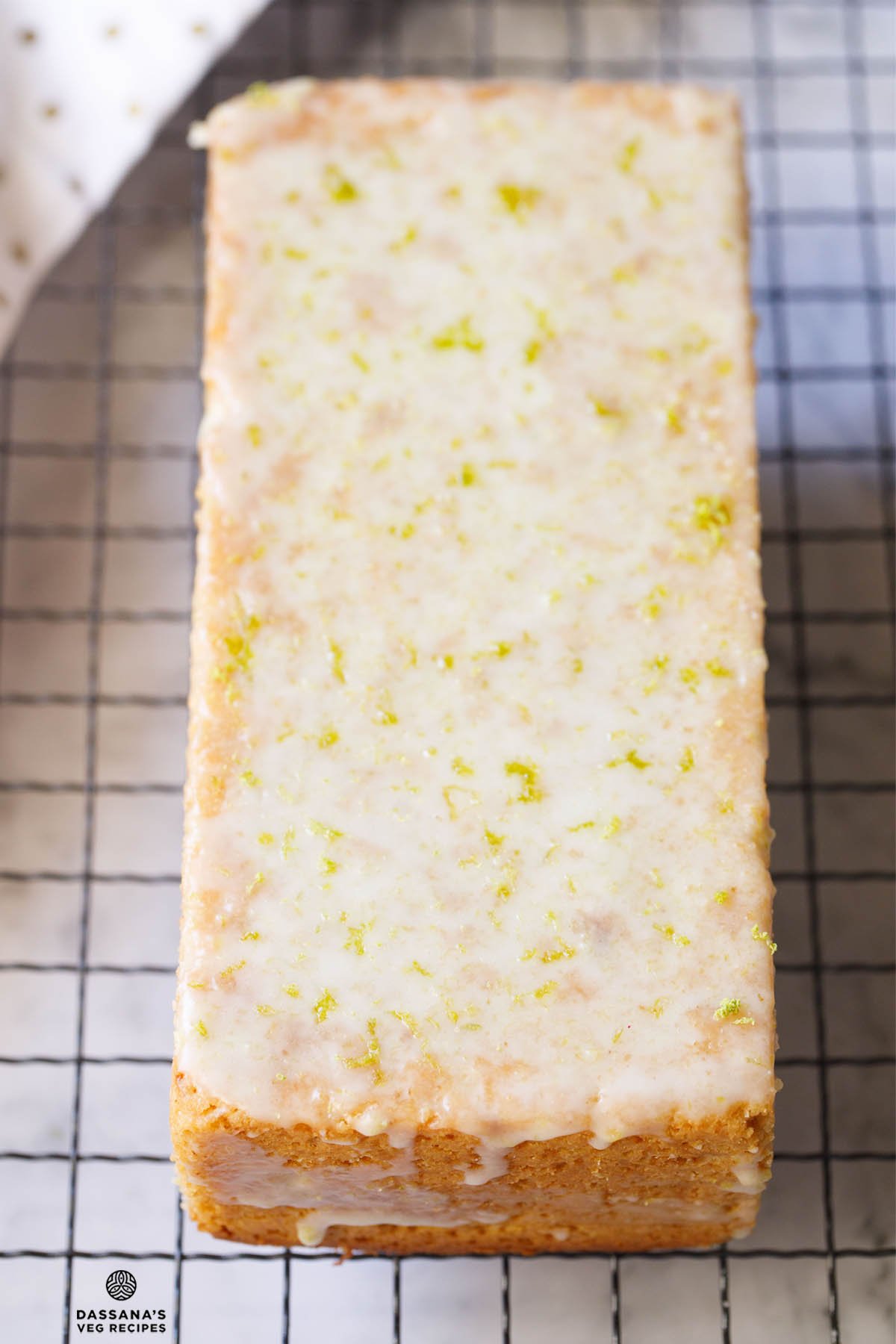 Glazed lemon drizzle cake loaf on wire rack.
