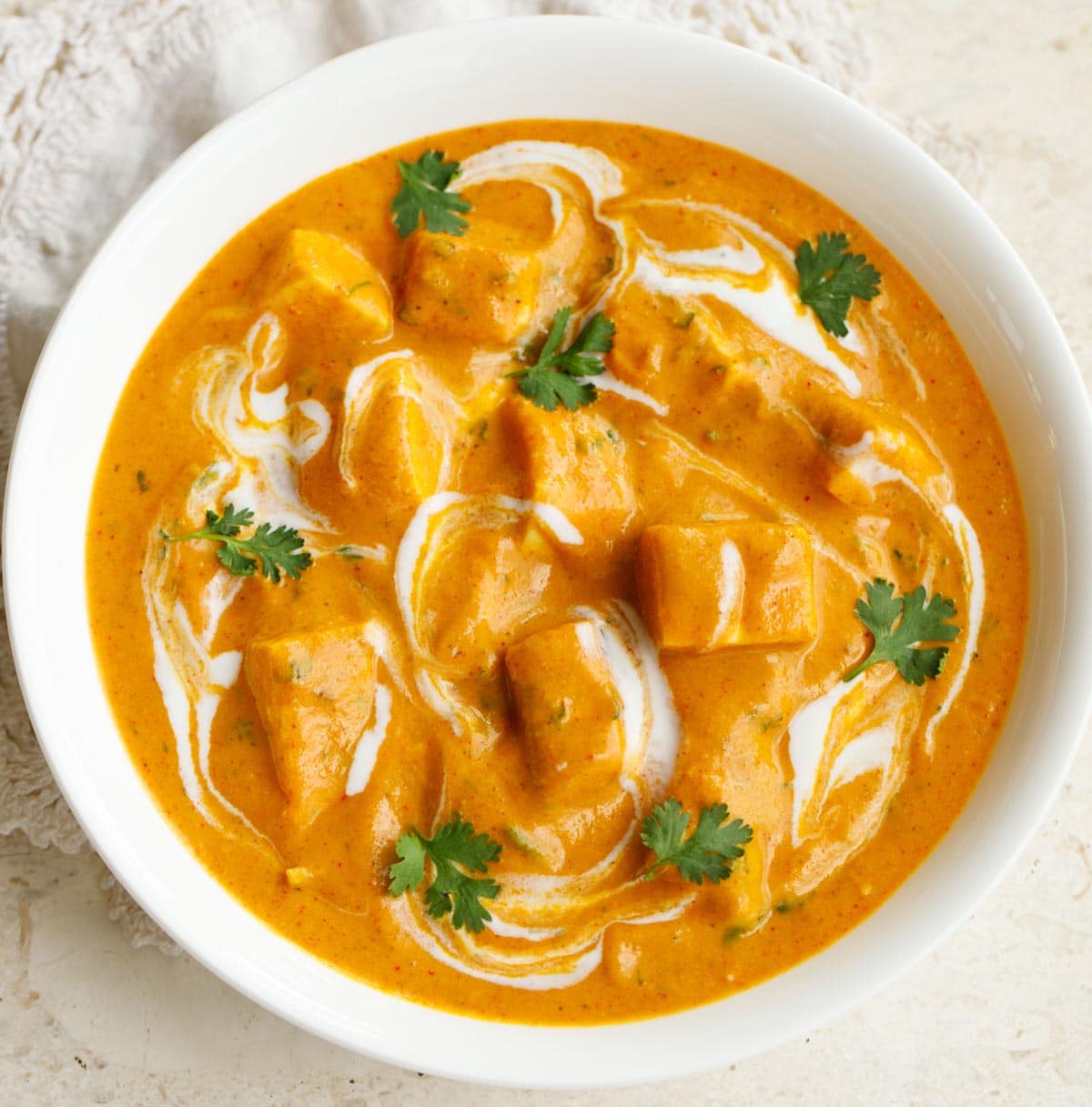 paneer angara in a white bowl garnished with coriander leaves and swirls of cream.