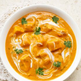 paneer angara in a white bowl garnished with coriander leaves and swirls of cream placed on an off-white doily.