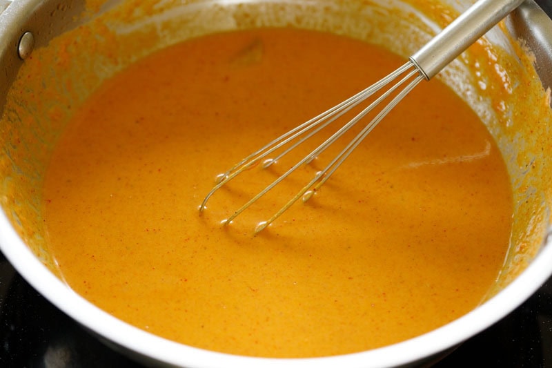 A whisk mixing water and the masala paste to an even gravy mixture.