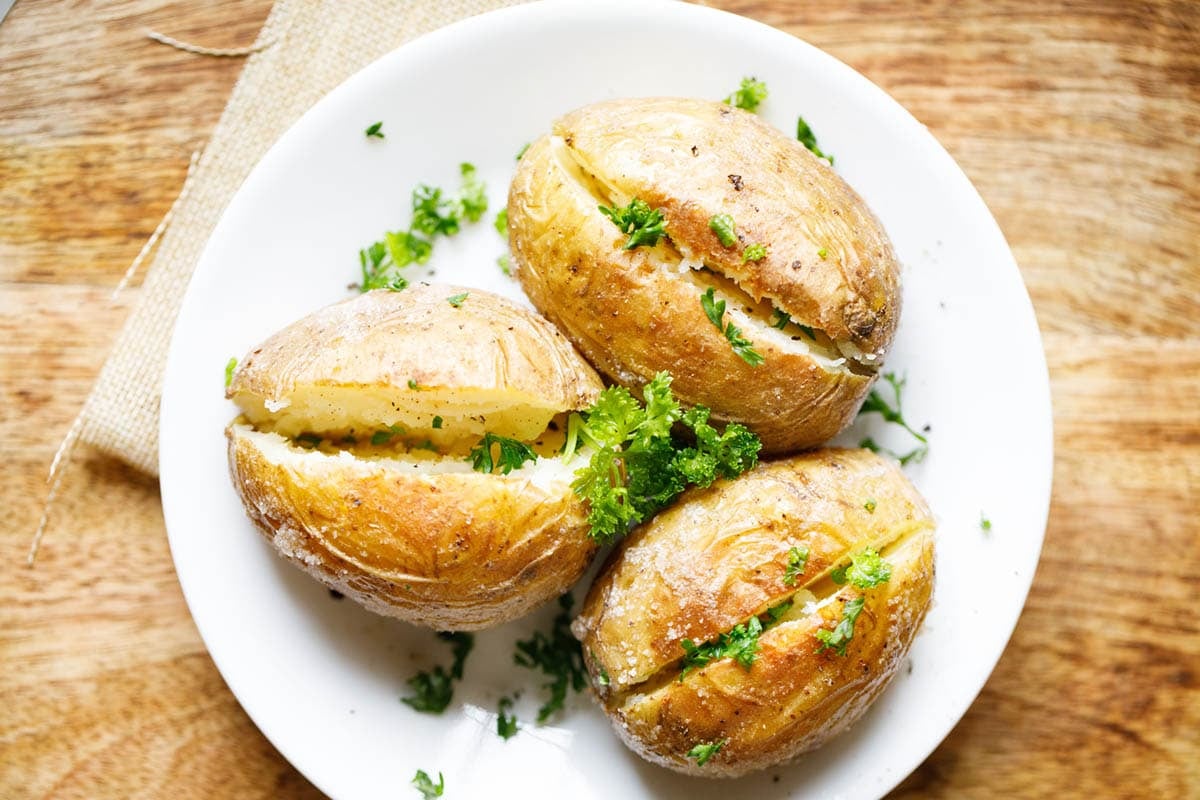 Three baked potato on white plate garnished with parsley.