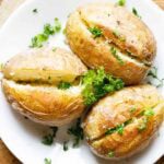 Three baked potato on white plate garnished with parsley and seasoned with black pepper.