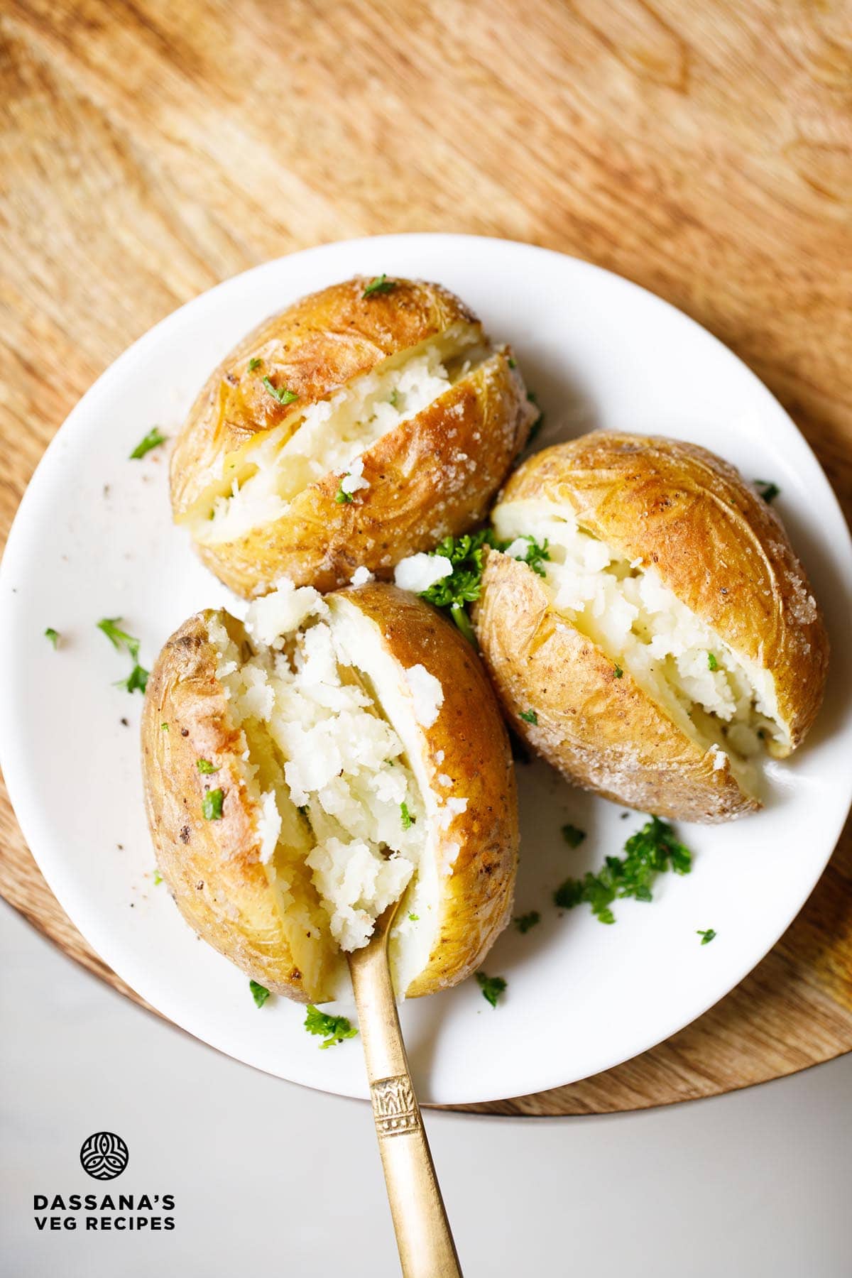 Baked potatoes on white plate with a fork showing the fluffy tender cooked potato.