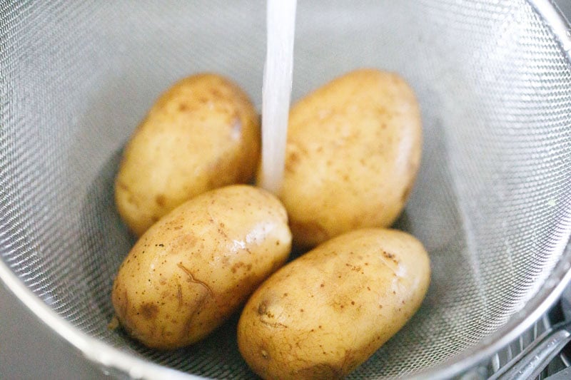 Potatoes being rinsed in strainer under tap water.