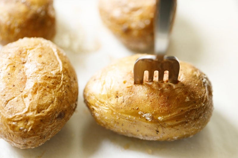 Baked potato being checked for doneness with a fork.