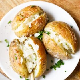 Baked potatoes on a plate with a fork showing the fluffy tender cooked potato.