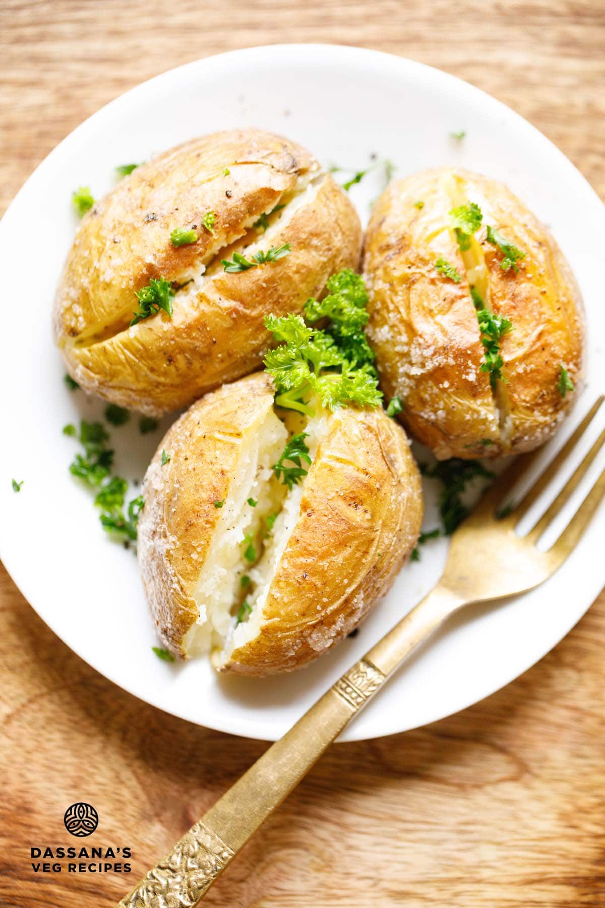 Baked potatoes on white plate garnished with parsley with a golden fork at the side.