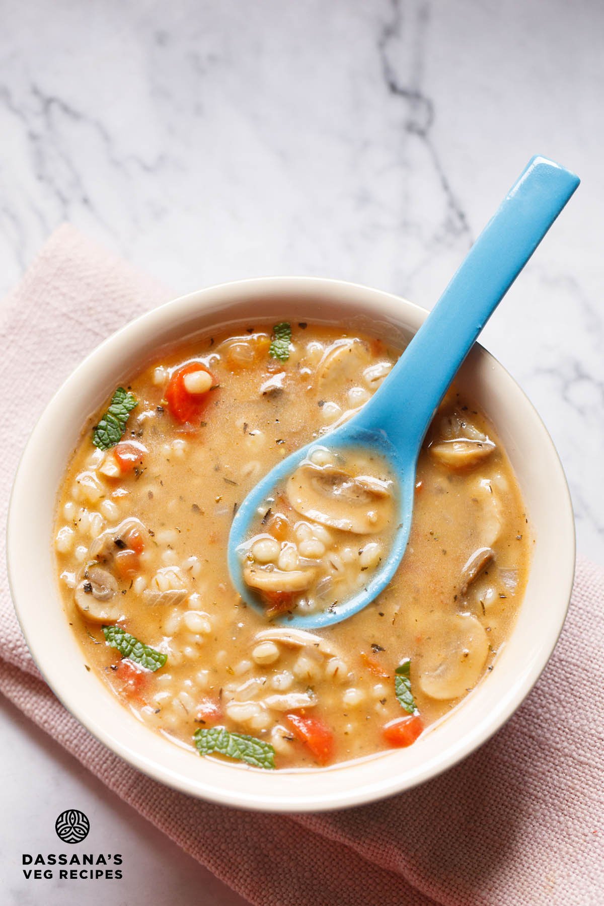 Barley soup in bowl with a blue spoon in center showing soup consistency.