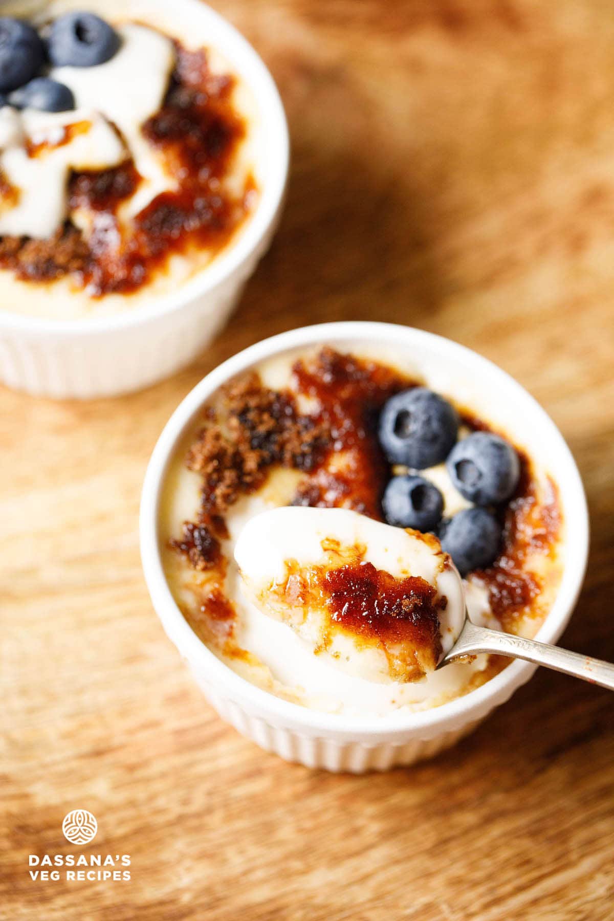 Crème Brûlée with a caramelized sugar top and a spoonful showing the creamy custard, garnished with fresh blueberries.