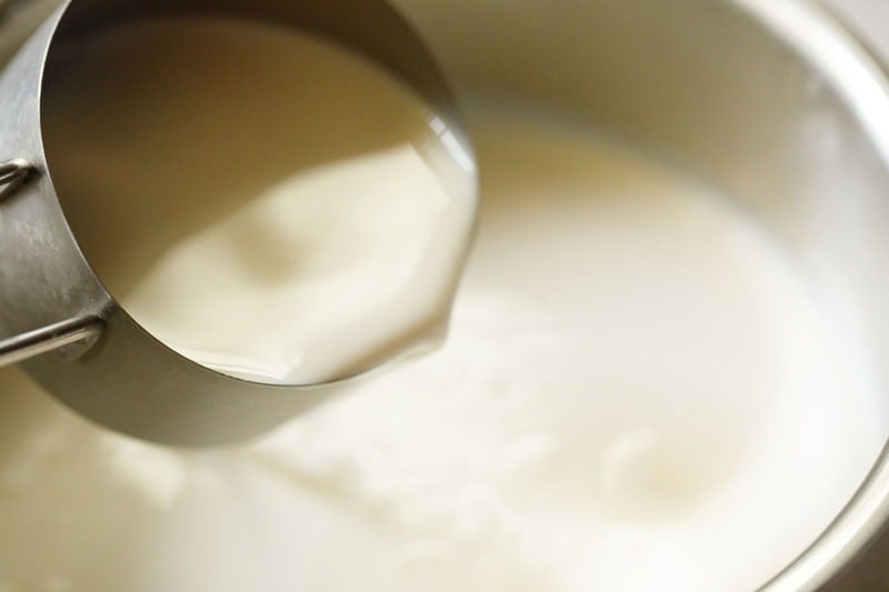 Milk being poured from measuring cup in a pan containing cream.