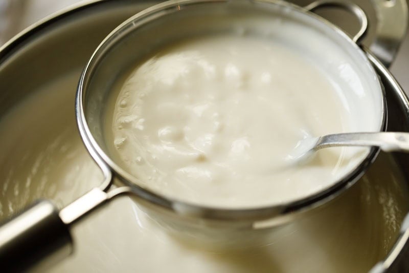 Straining thickened custard through a mesh strainer.