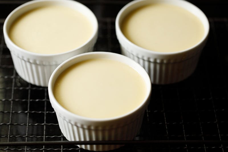 Baked creme brulee in ramekins on wired rack.