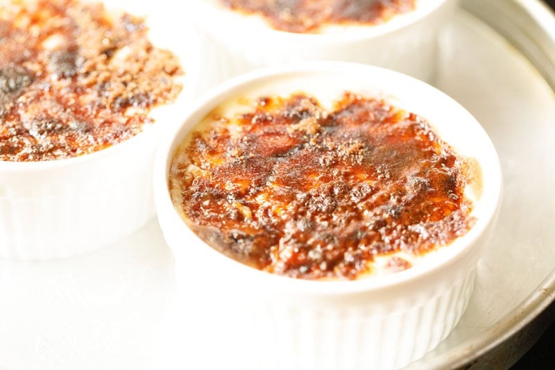Close-up of crème brûlée with a caramelized sugar crust in white ramekins after broiling.