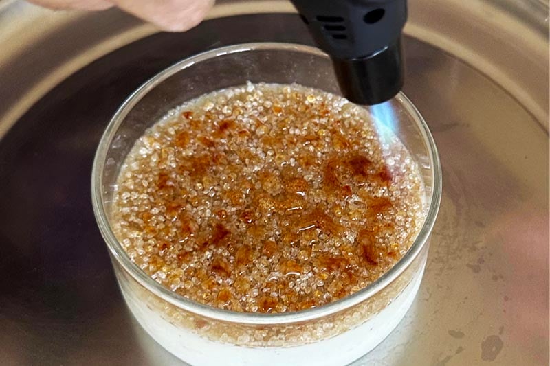 Torch caramelizing the sugar layer on crème brûlée, creating an even golden brown crust.
