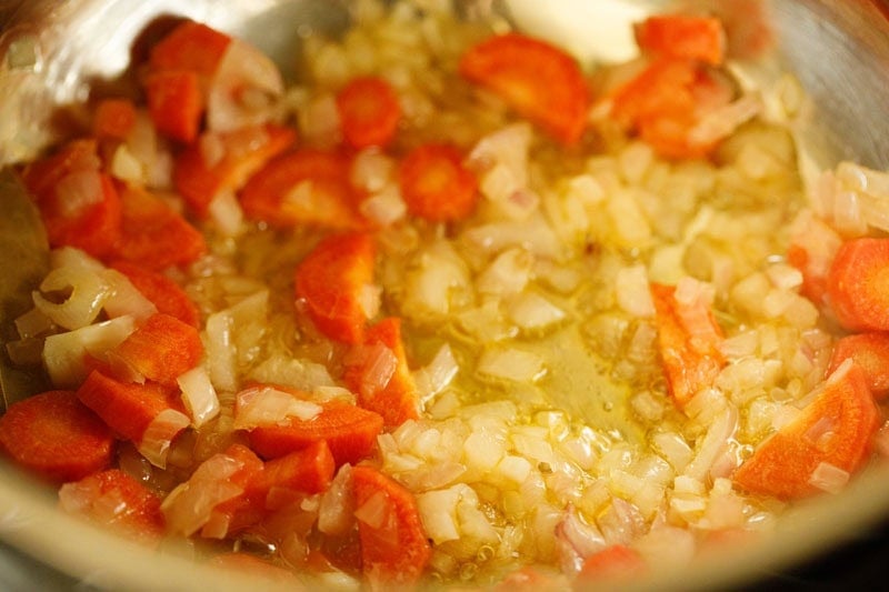 Onions and carrots being sautéed in pan.