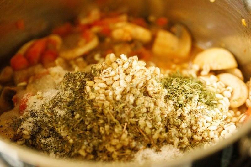 Rinsed pearl barley with dried herbs and seasonings in pan.