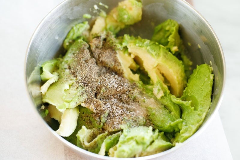 Sliced avocado and seasonings in a bowl.
