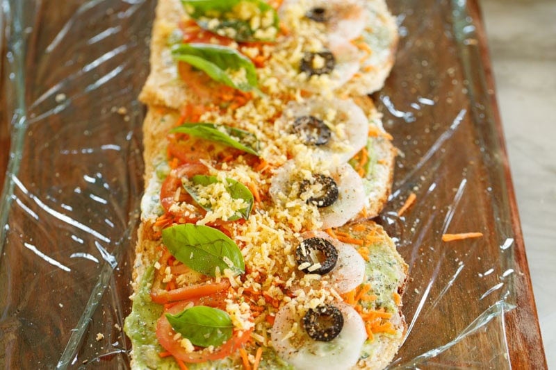 Colorful toppings on bread slice placed vertically on cling film for easy rolling.