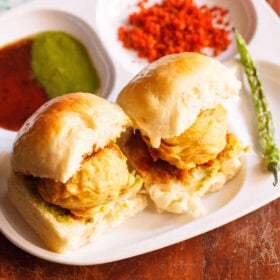 Two vada pav with chutneys and fried green chilli.