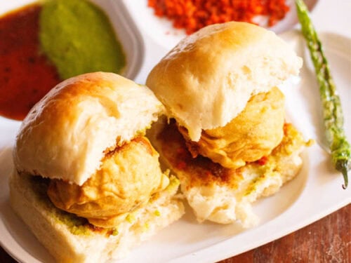 Two vada pav with chutneys and fried green chilli.