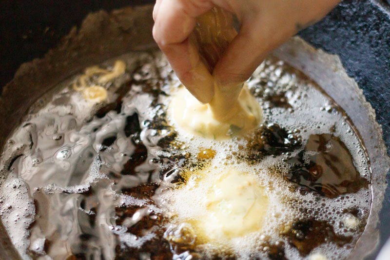 adding gram flour batter coated potato balls in hot oil to make vada pav. 