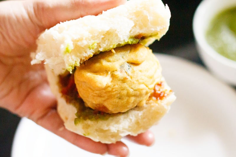 Hand holding a vada pav sandwich.