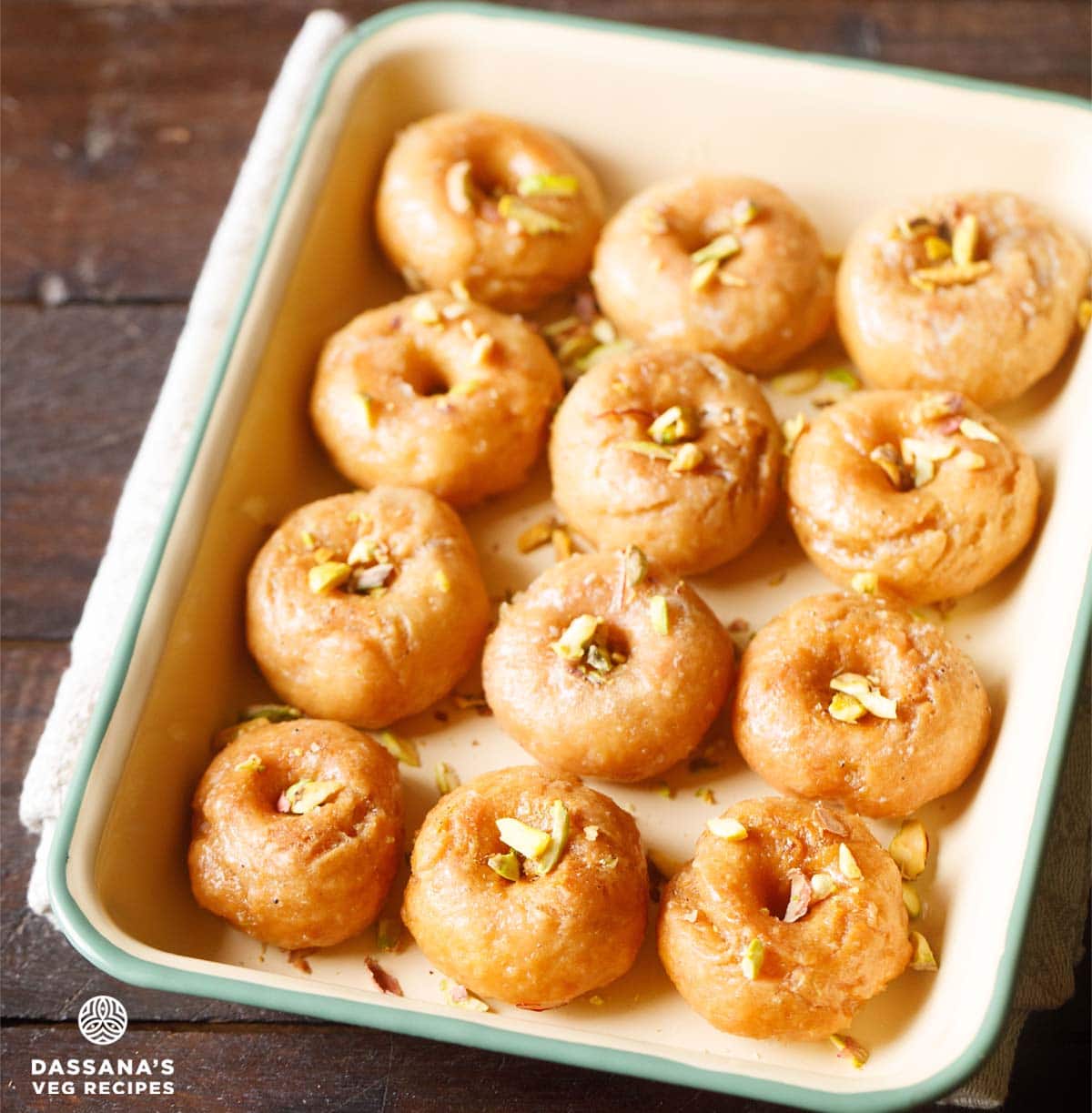 balushahi or badusha garnished with chopped pistachios and served in a ceramic tray.