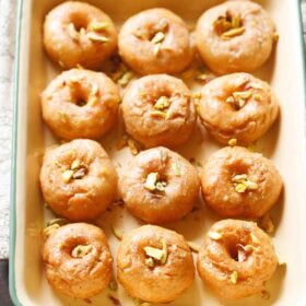 balushahi garnished with chopped pistachios and served in a ceramic tray.
