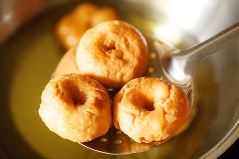 removing fried balushahi recipe from hot oil with a slotted spoon.