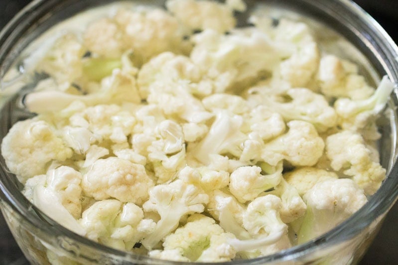 Chopped cauliflower soaked in water in a glass bowl.