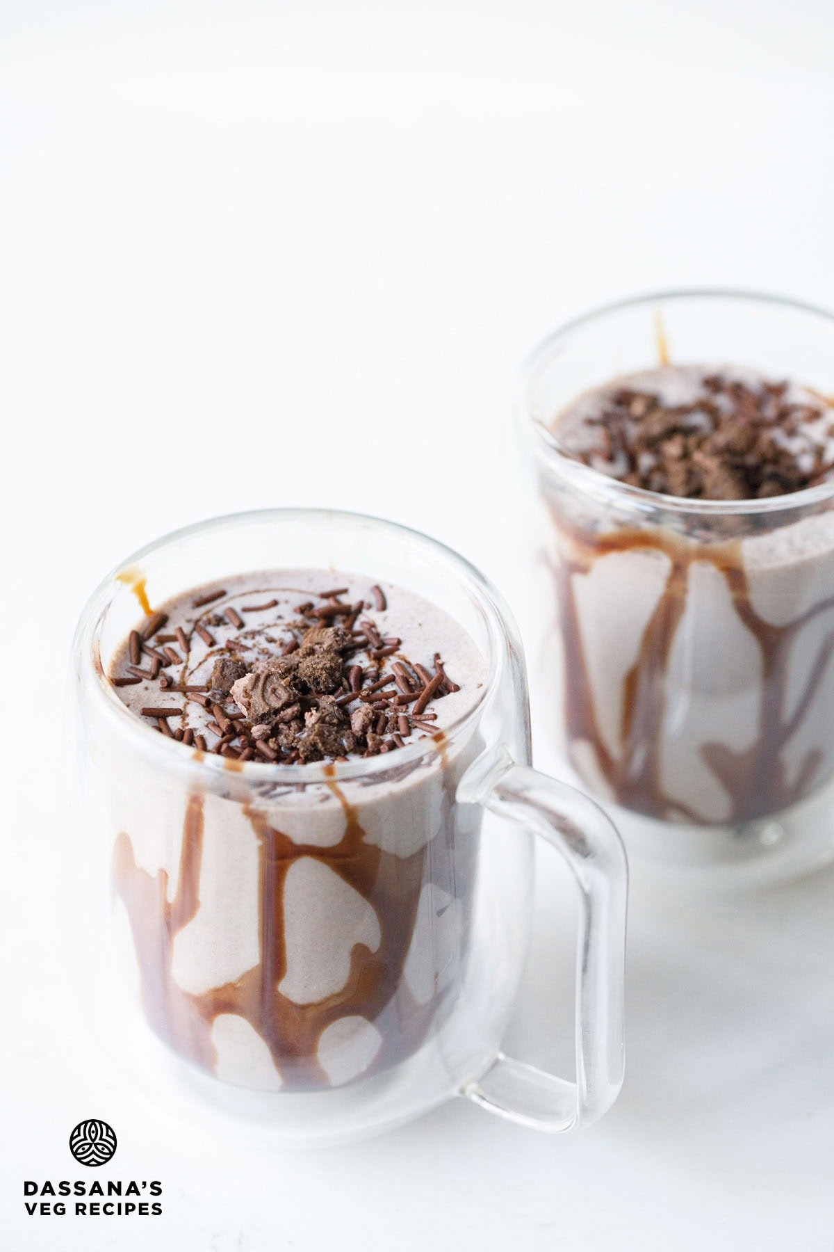 Cafe style Oreo milkshake with toppings in two clear glasses.