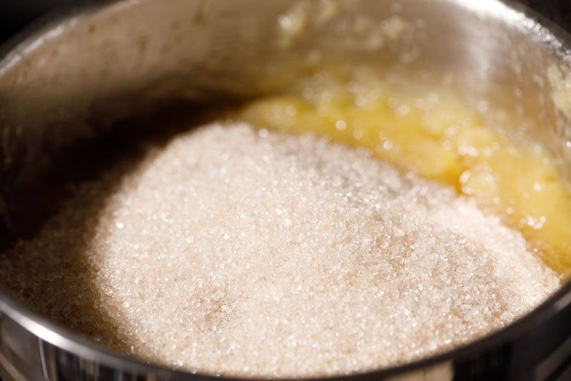 Mound of sugar on mashed apples in pan.