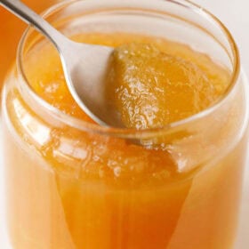 Scooping apple jam on a spoon in a jar.