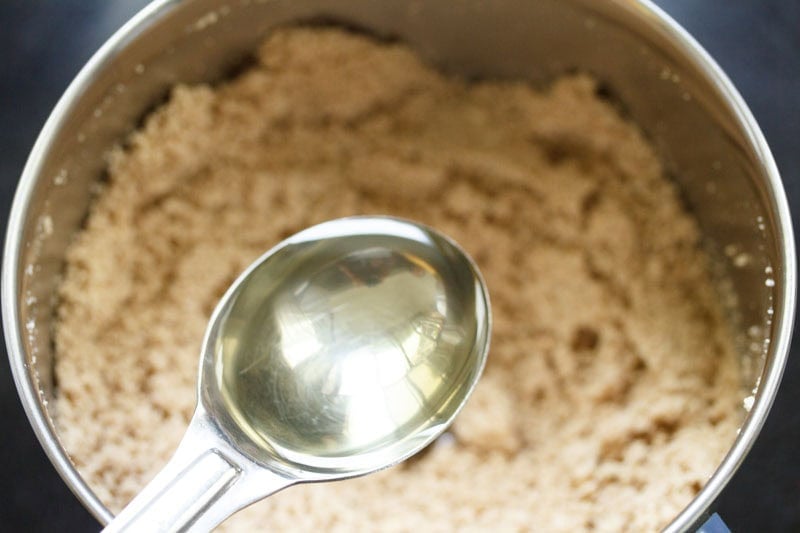 Spoon with oil above ground sesame seeds in blender.