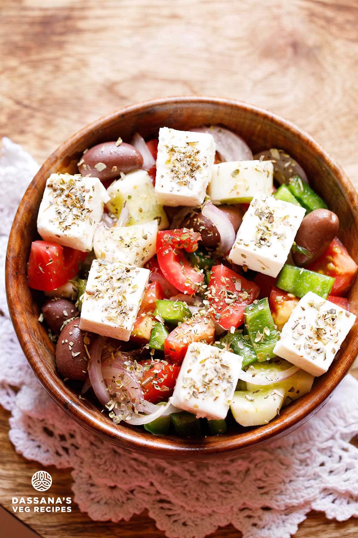 Colorful Greek salad with feta cheese cubes in wooden bowl.