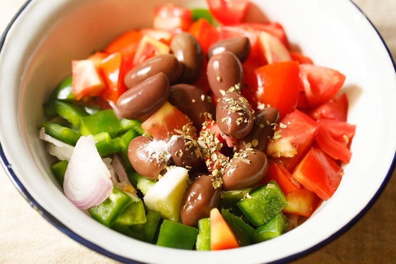 Salt and oregano on vegetables and olives in bowl.