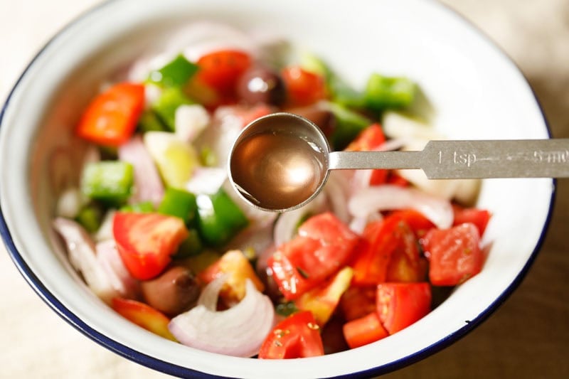 Fresh vegetables in a bowl with red wine vinegar being added.