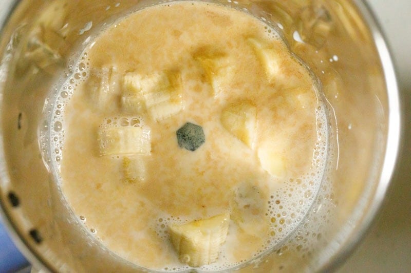 Blender with chopped banana, milk and vanilla inside.