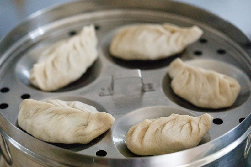 Paneer momo dumplings in a tray placed inside a steamer pan.